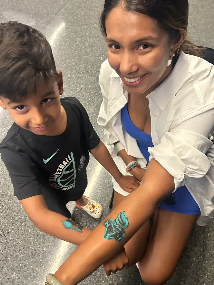 Boy and woman display matching blue temporary tattoos on their arms, smiling at the camera.