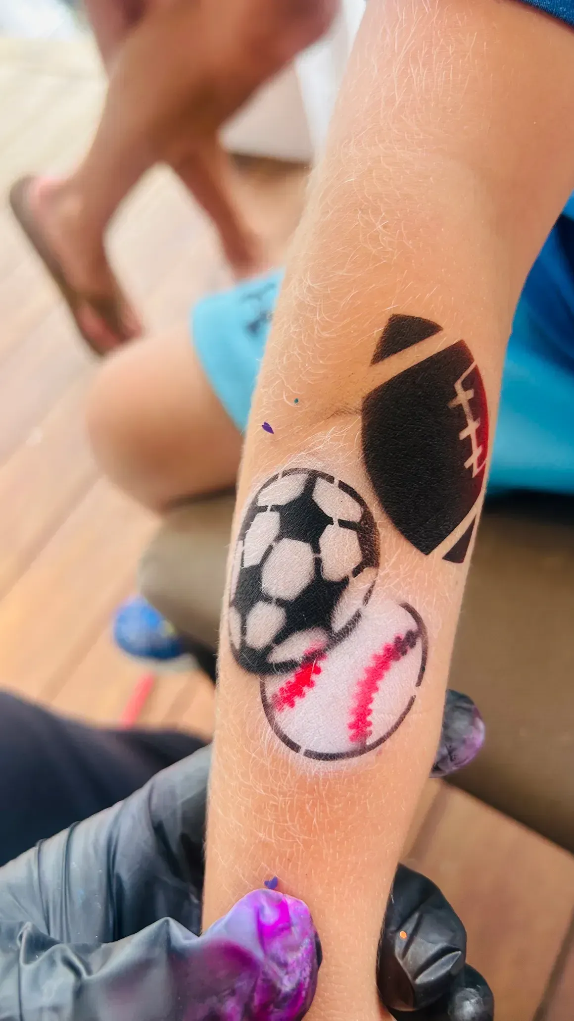 Sports-themed temporary tattoos applied on a child's arm; soccer ball, football, and baseball designs.