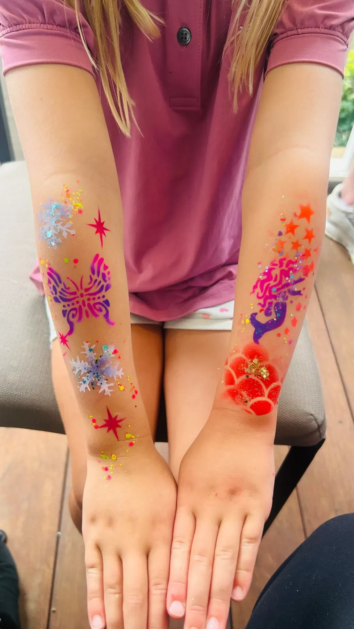 Arms with colorful temporary tattoos of flowers, butterflies, and a mermaid.