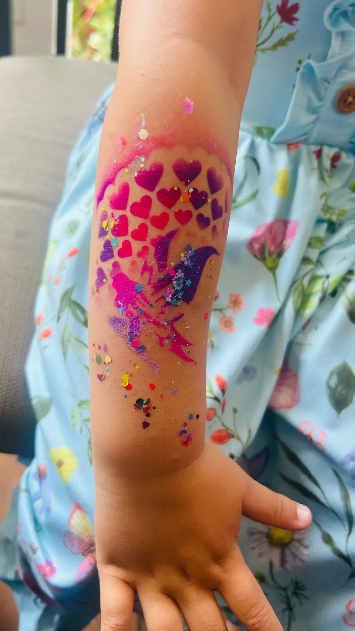 Child's arm with a temporary tattoo of two birds and hearts in pink, purple, and glitter.