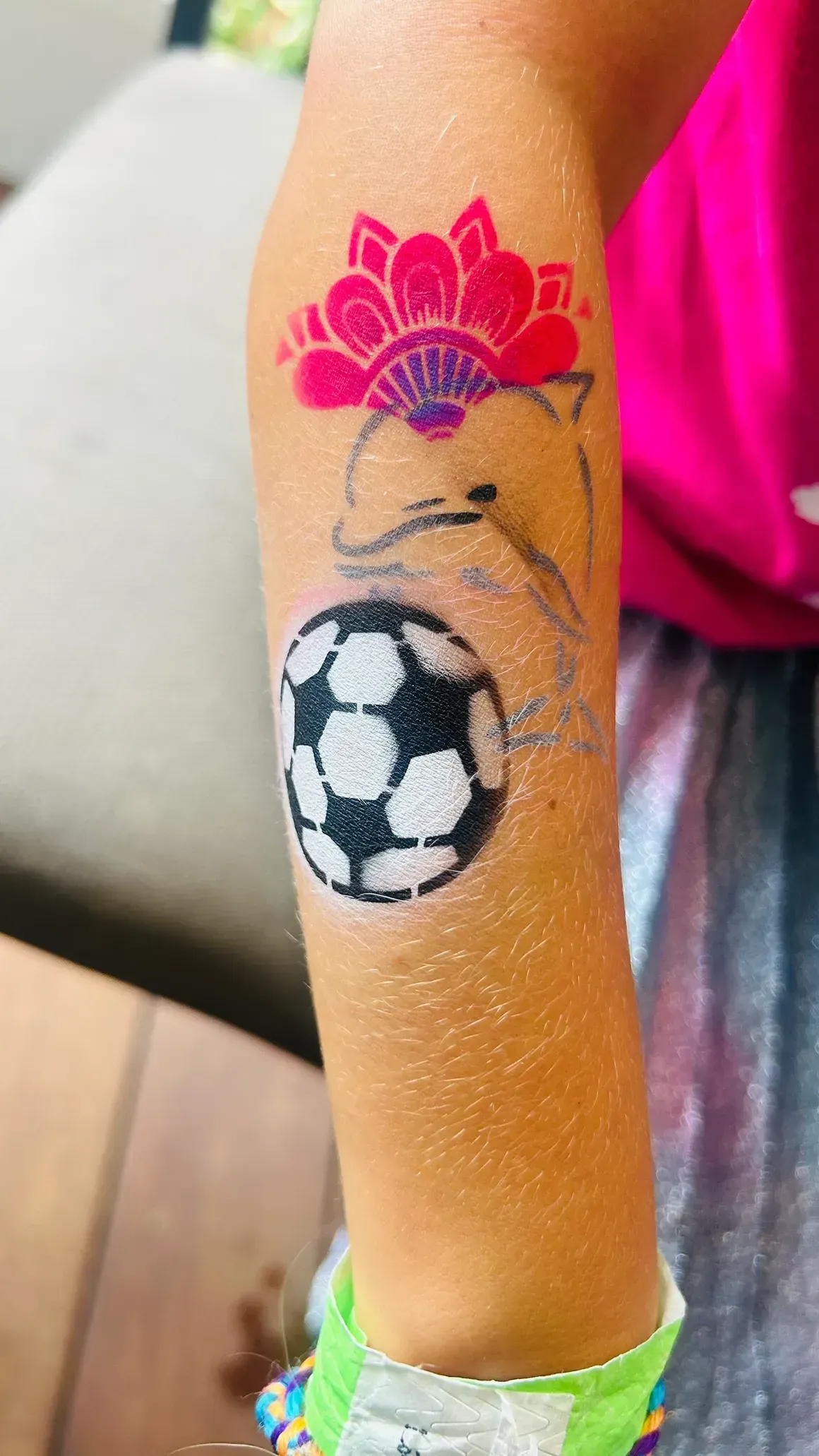 Arm with temporary tattoos: flower, dolphin, and soccer ball. Pink shirt and silver skirt visible.