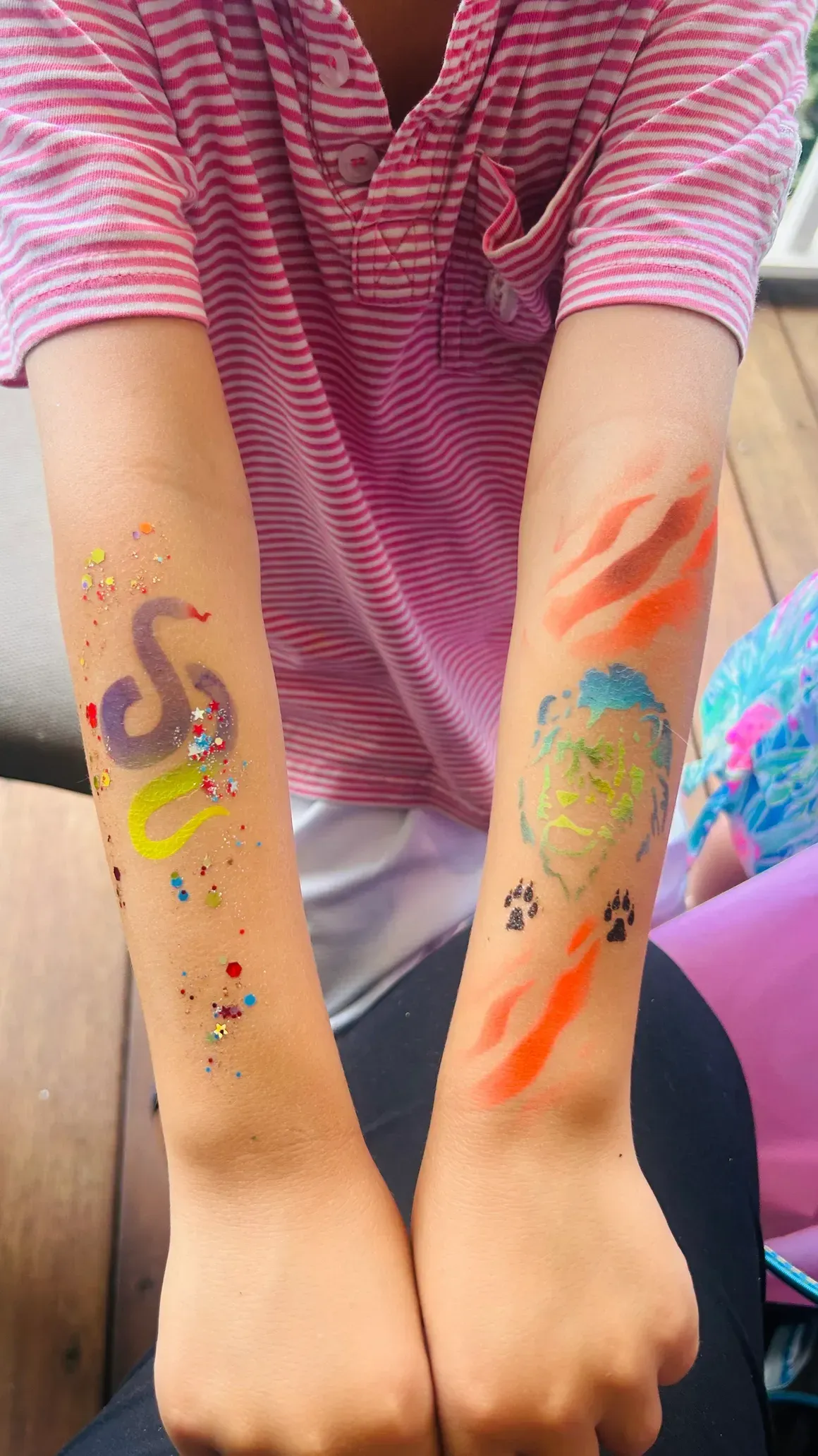 Arms with temporary tattoos: snake and abstract design. Pink shirt, outdoor setting, glitter.