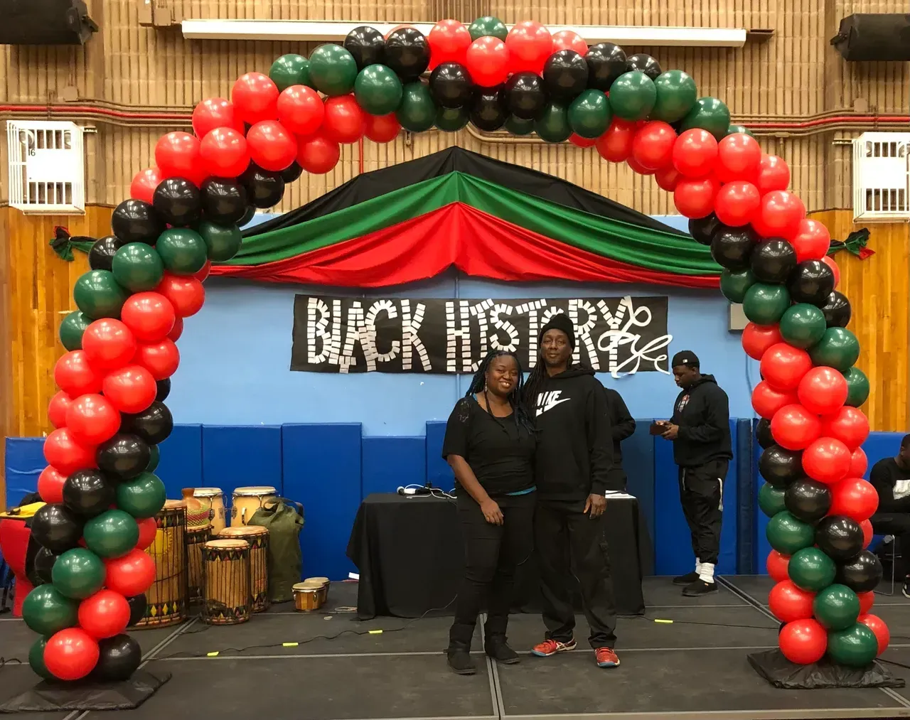 A group of people standing under a red , green and black balloon arch.