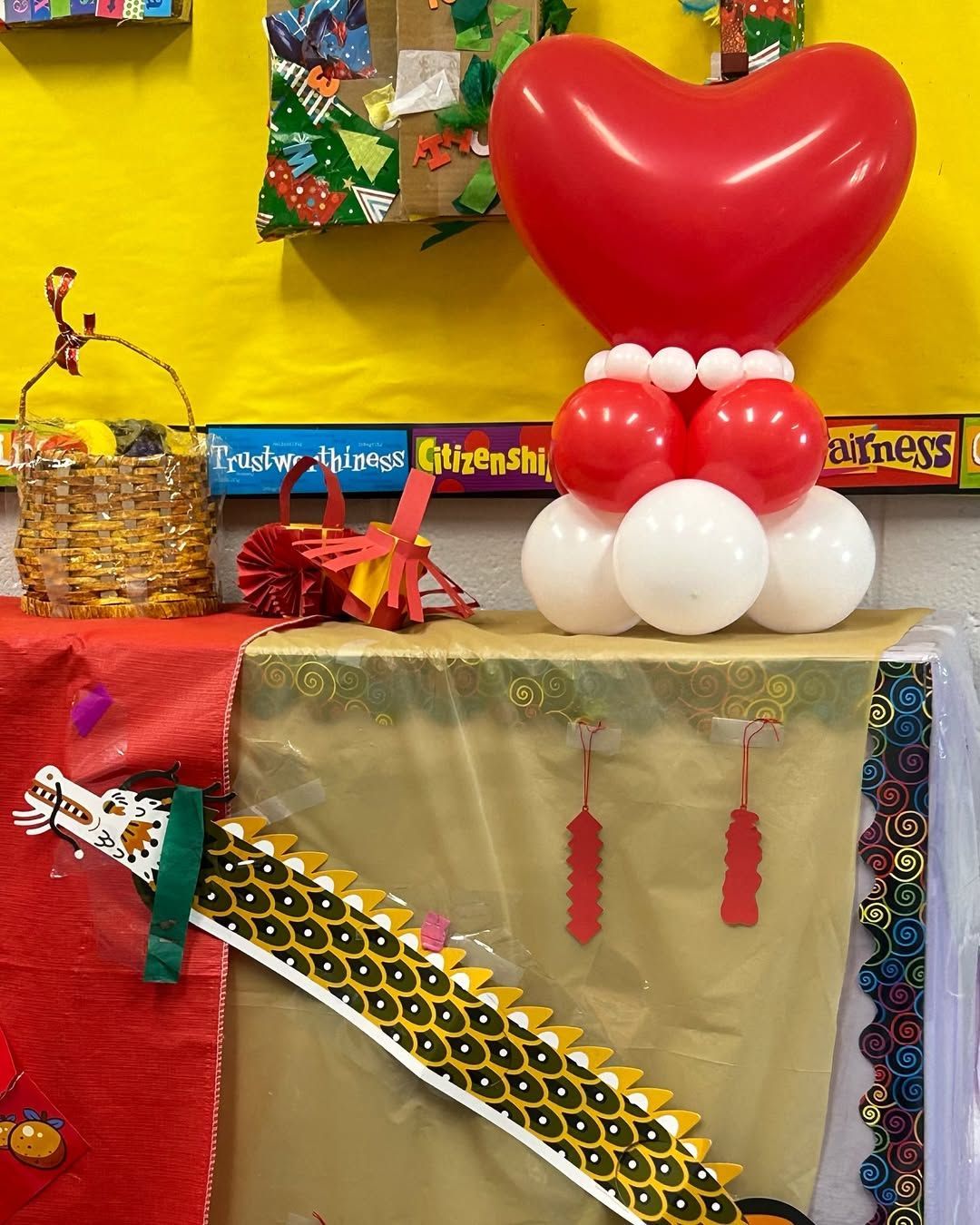 Red heart balloon sculpture atop other balloons, on a display table with decorations.