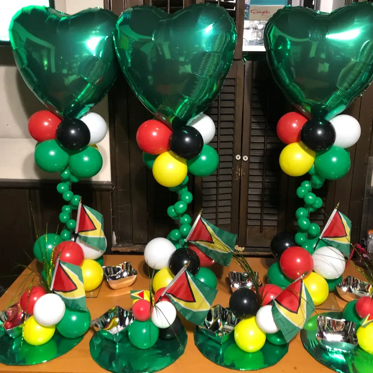 Three Guyana flag-themed balloon centerpieces with heart-shaped tops and mini flags.