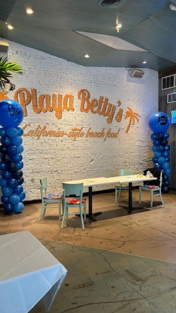 Playa Betty's restaurant interior with a table set for dining, flanked by blue balloon columns, and logo on the wall.