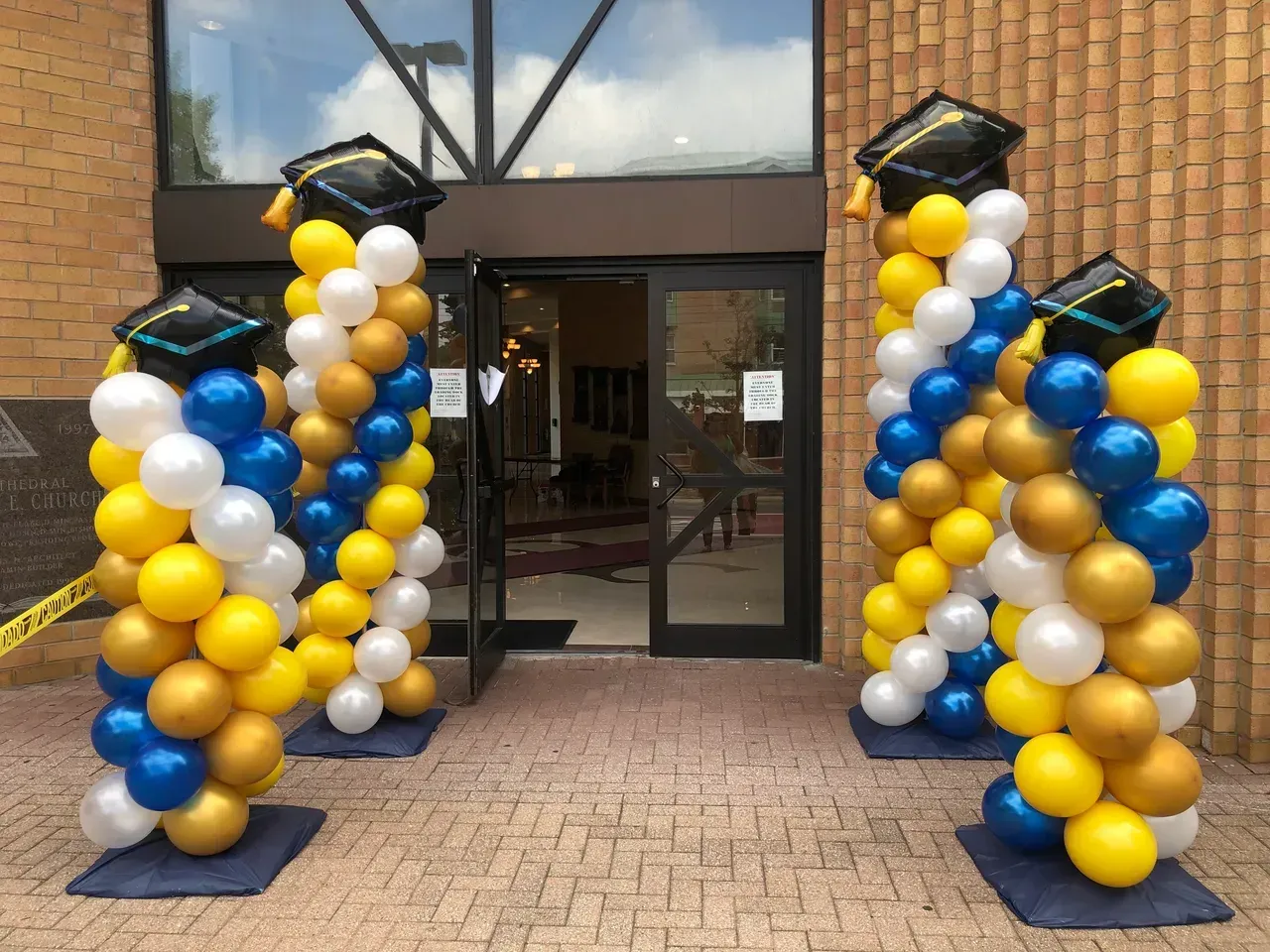 Two columns of balloons with graduation caps on them are in front of a building.