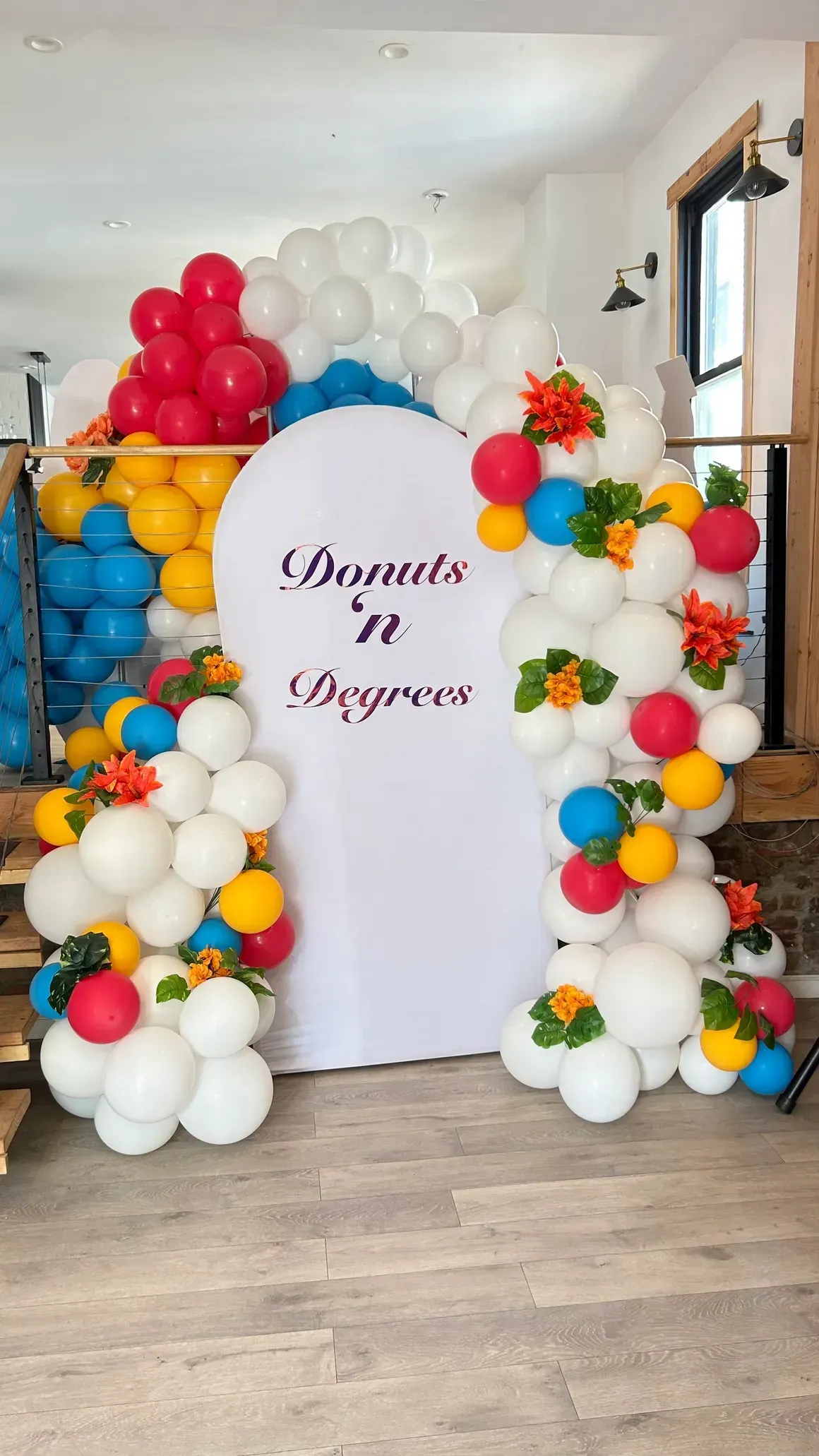 Colorful balloon archway with white backdrop; text reads