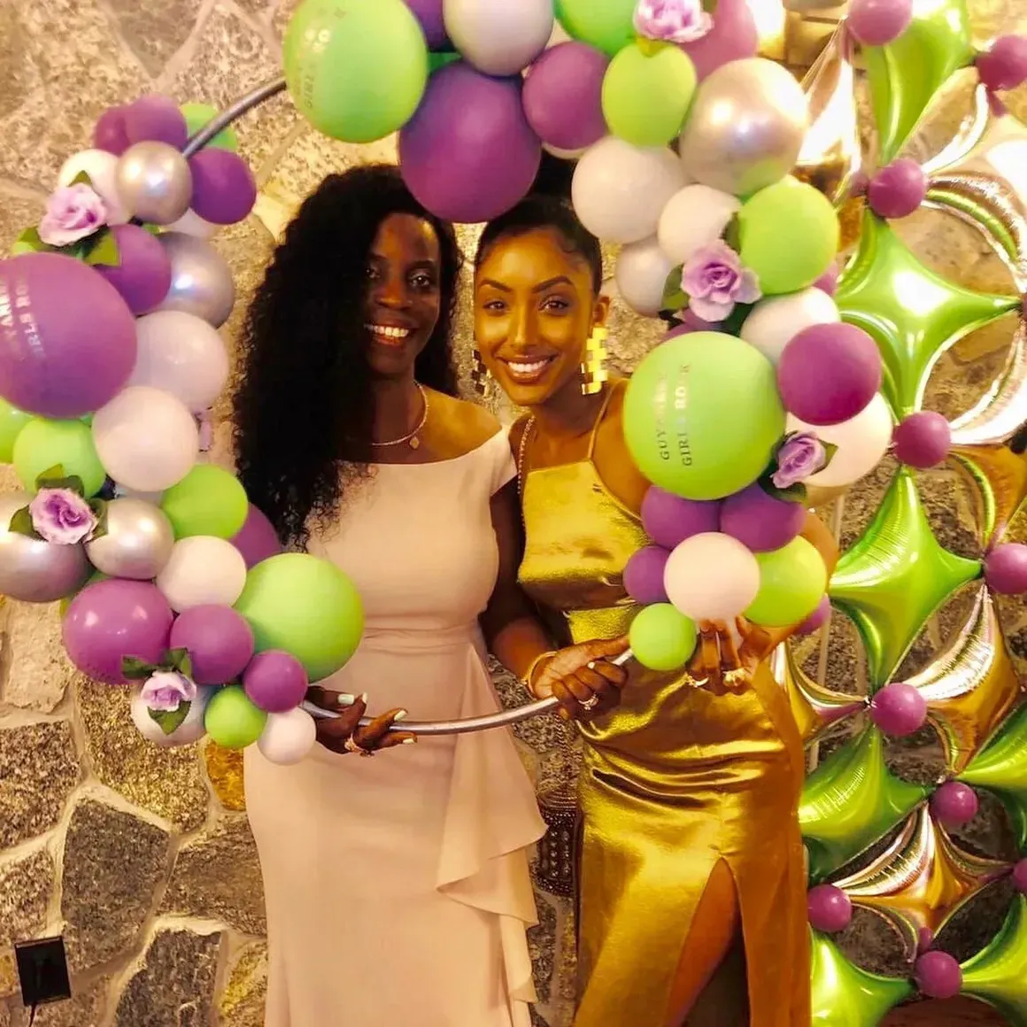 Two women are holding balloons in front of a wall