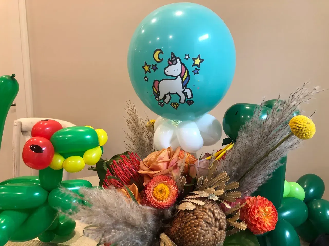 Balloon arrangement: turquoise unicorn balloon, floral display, and balloon dinosaur.
