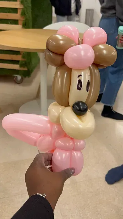 Balloon dog sculpture held by a person. Brown, pink, and beige colors; indoor setting.