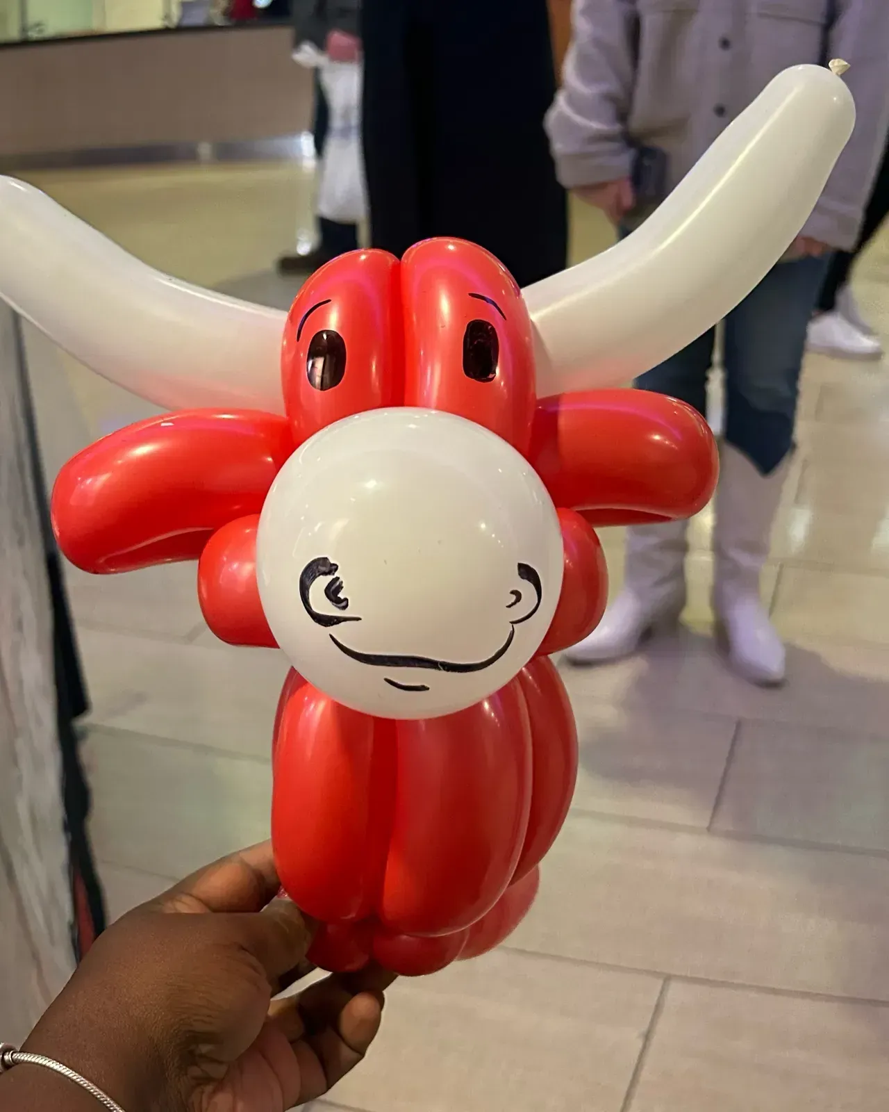 A red and white balloon sculpture of a bull being held by a hand.