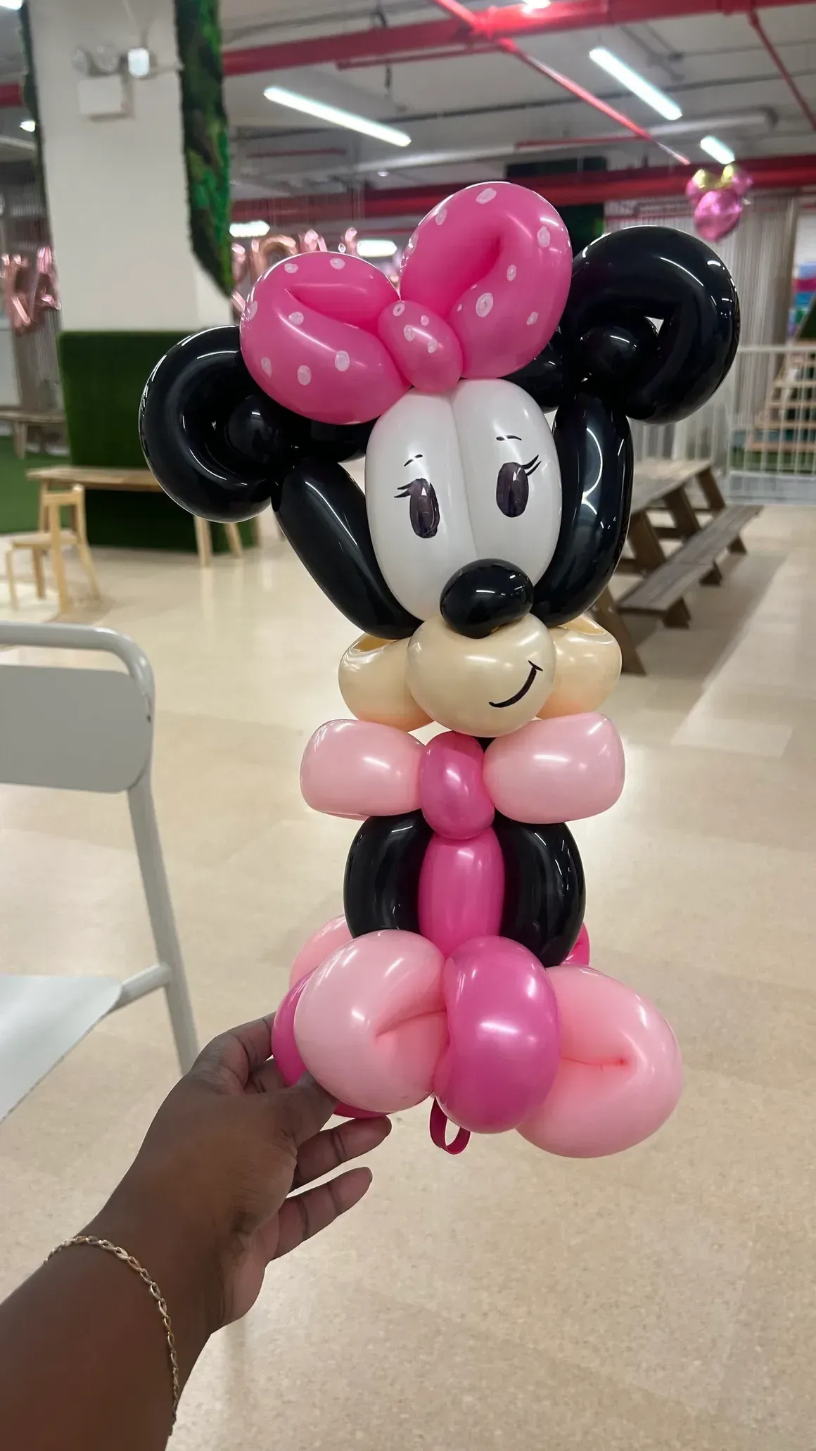 Minnie Mouse balloon sculpture, pink and black, held by a person in a room.