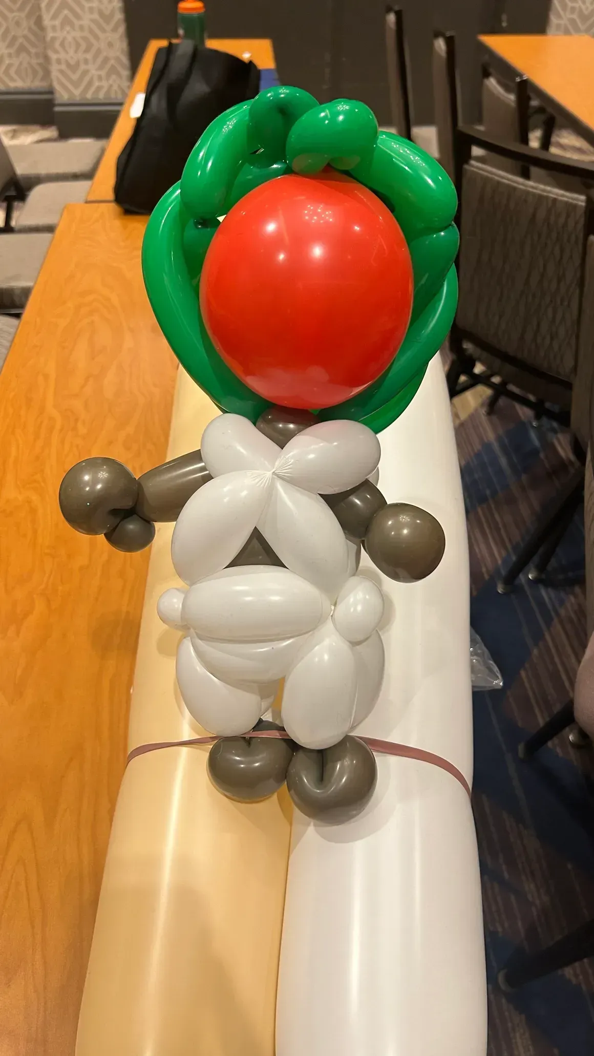 Balloon sculpture of a person with a red head and a green leafy crown, on a table.