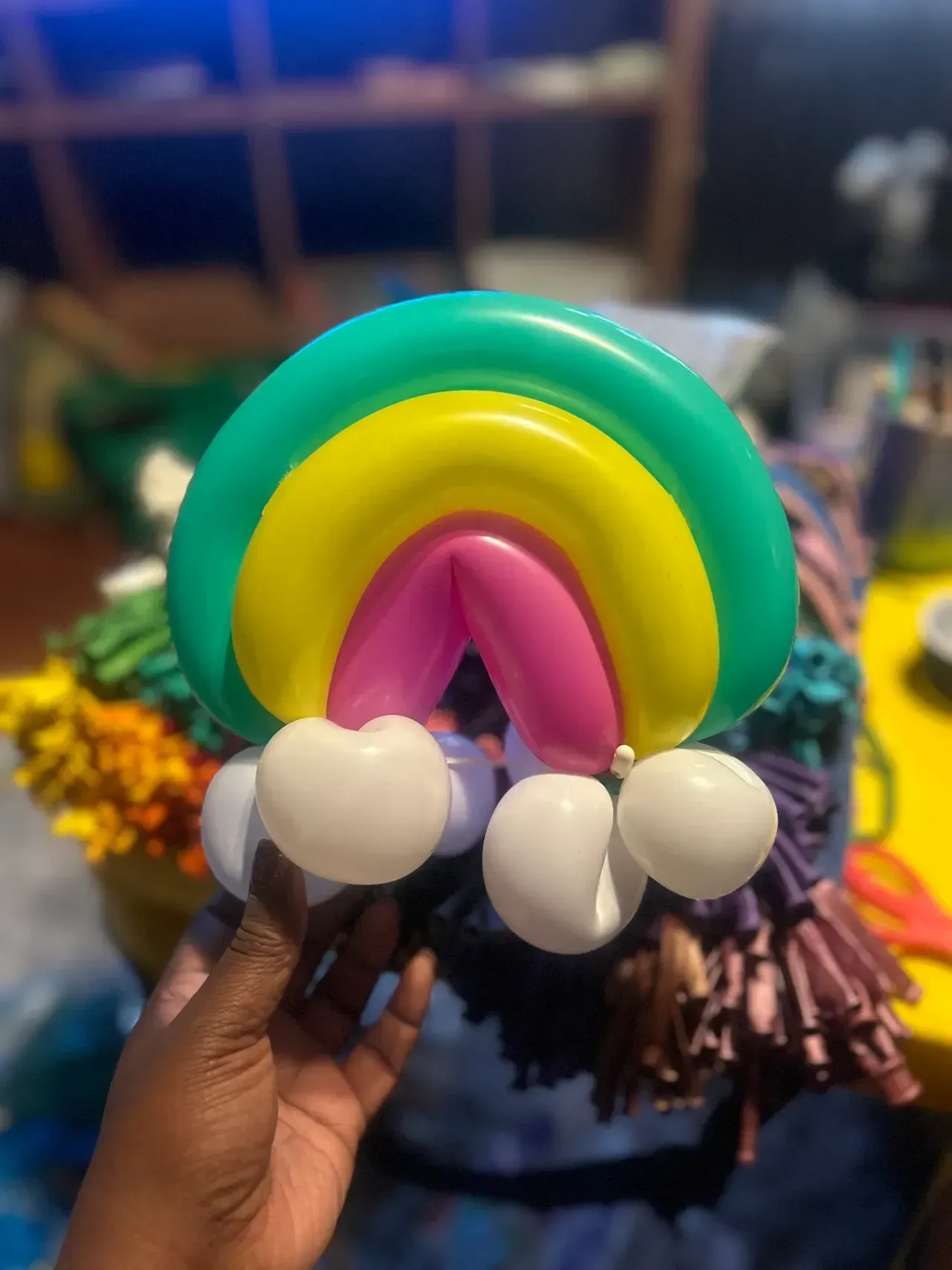 Person holding a balloon sculpture of a rainbow with white puffy clouds.