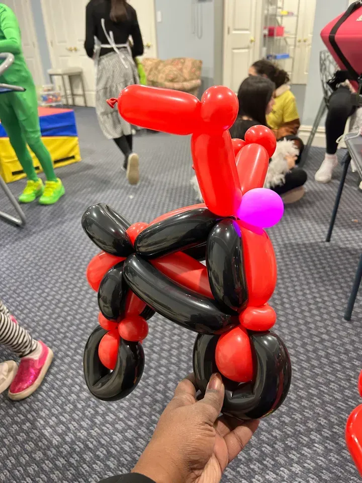 A person holding a red and black balloon motorcycle in a room with other people.
