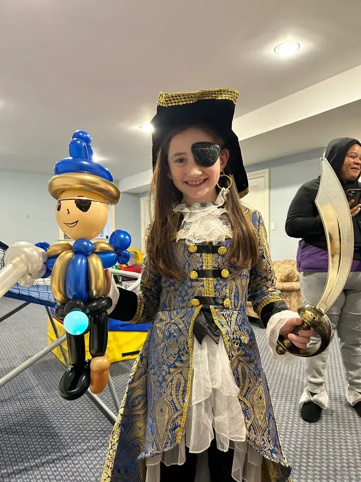 Girl in pirate costume holding a balloon figure, with a sword.