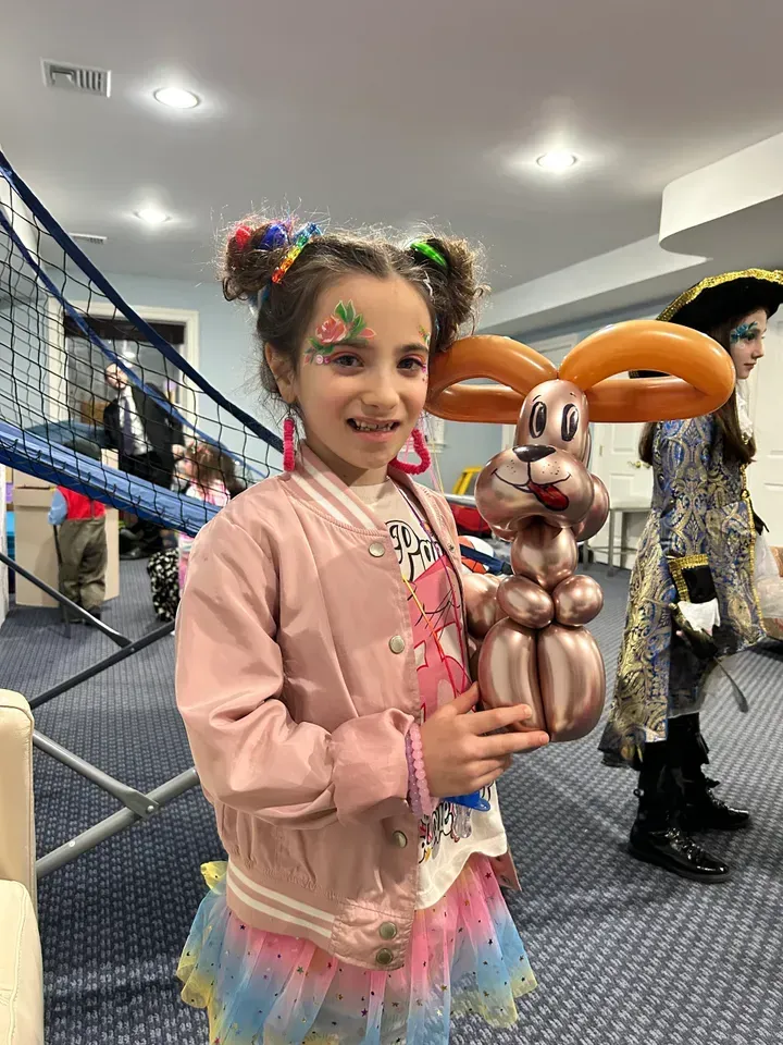 Girl with colorful hair and face paint holding a rose gold balloon bunny.