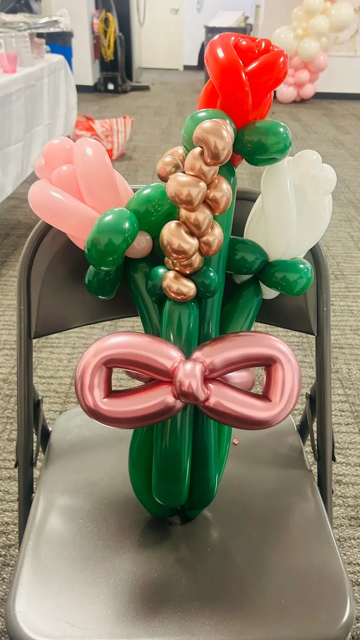 Balloon bouquet of pink, red, and white flowers tied with a pink bow, sitting on a folding chair.