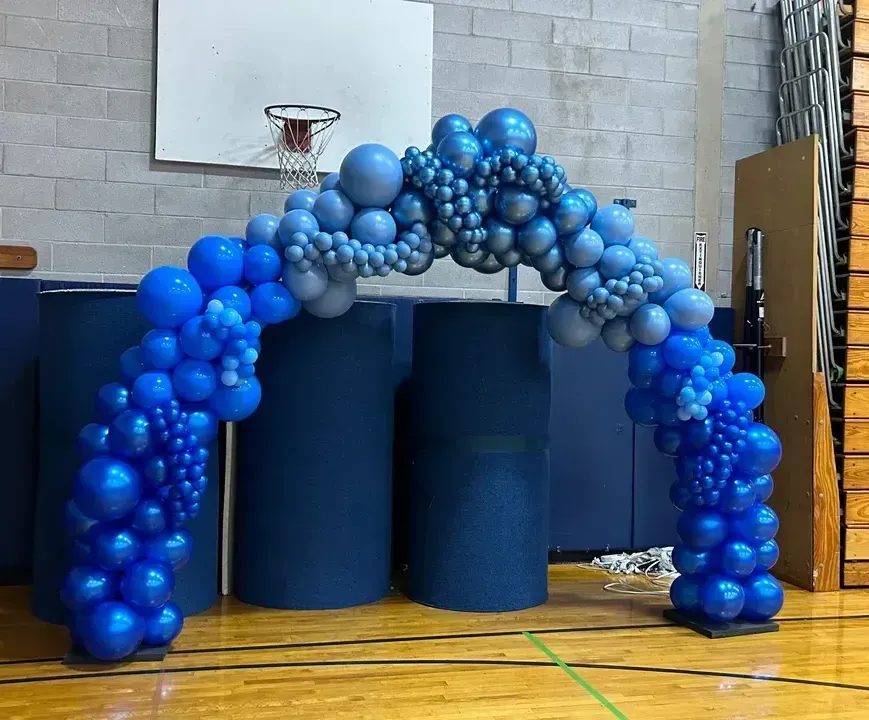 Blue balloon arch over a doorway in a gym.
