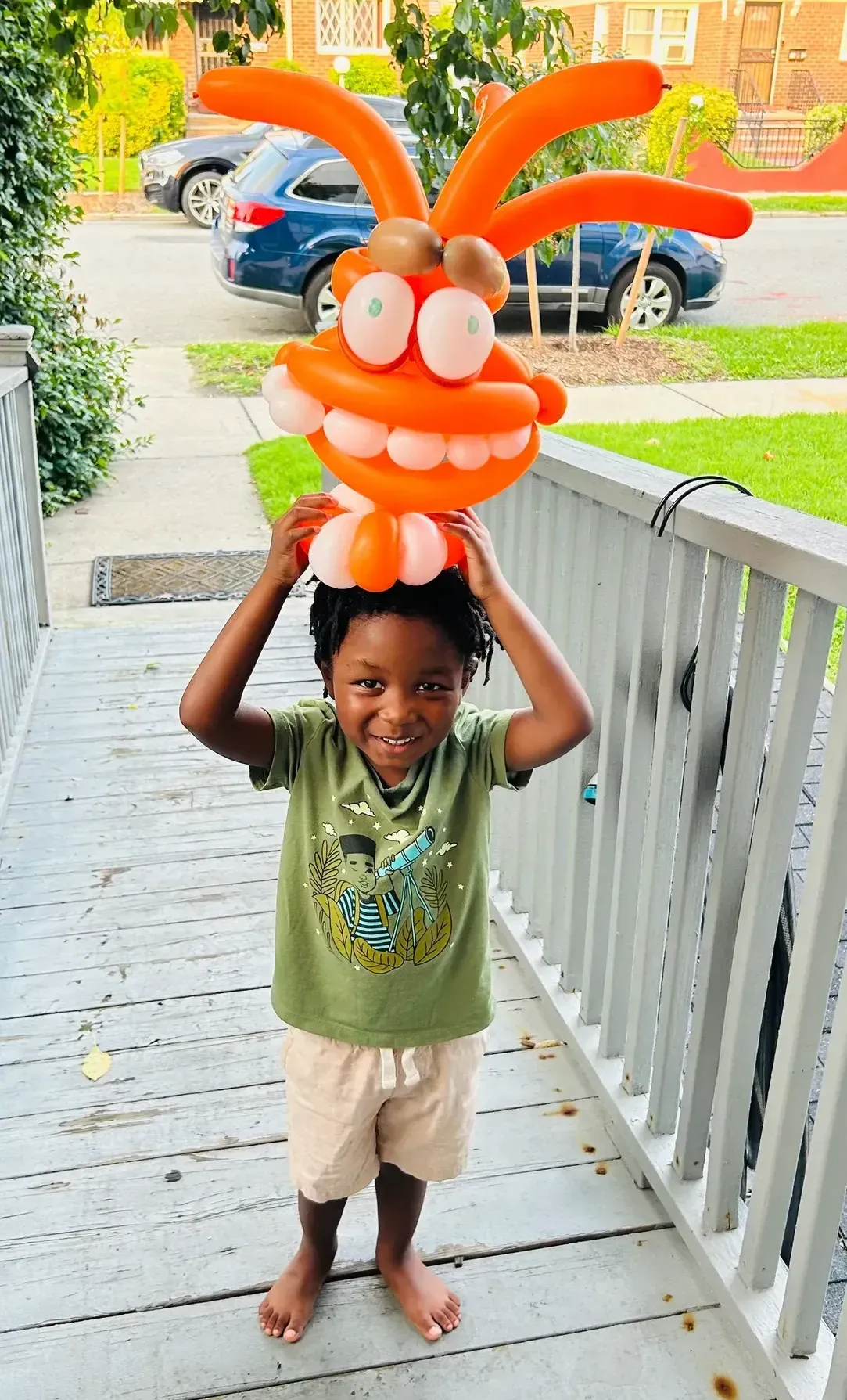 Boy holding up a large orange balloon sculpture on a porch.