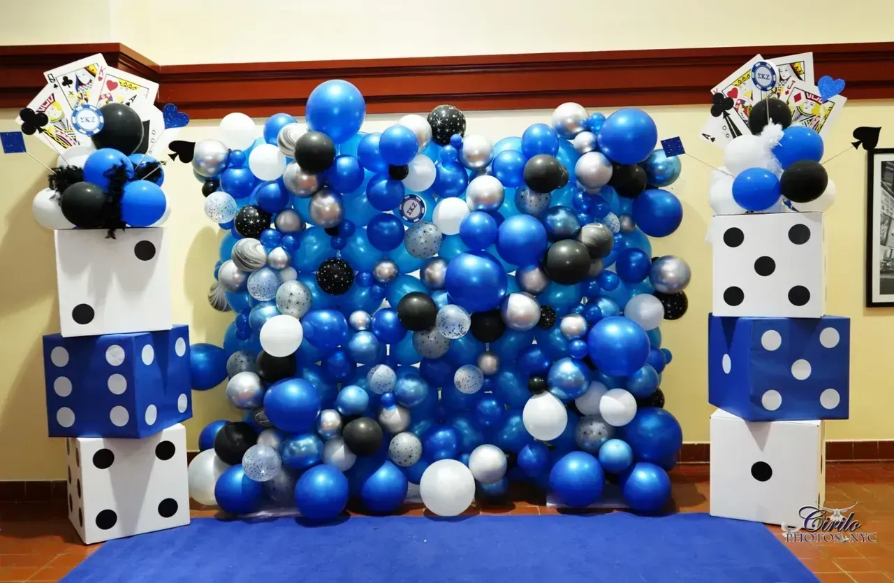 Blue, white, black, and silver balloon backdrop with dice-themed decorations for an event.