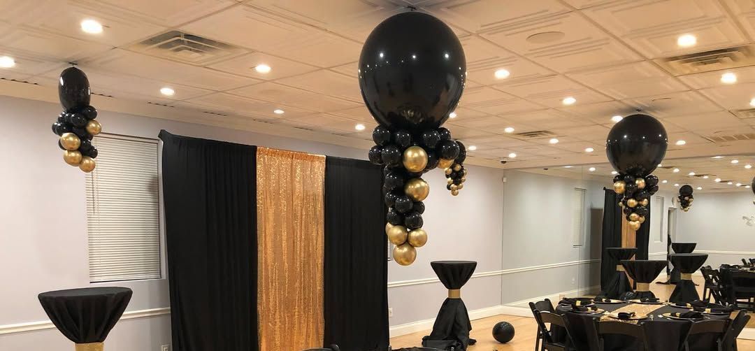 Decorated event space with black and gold balloons and table settings.