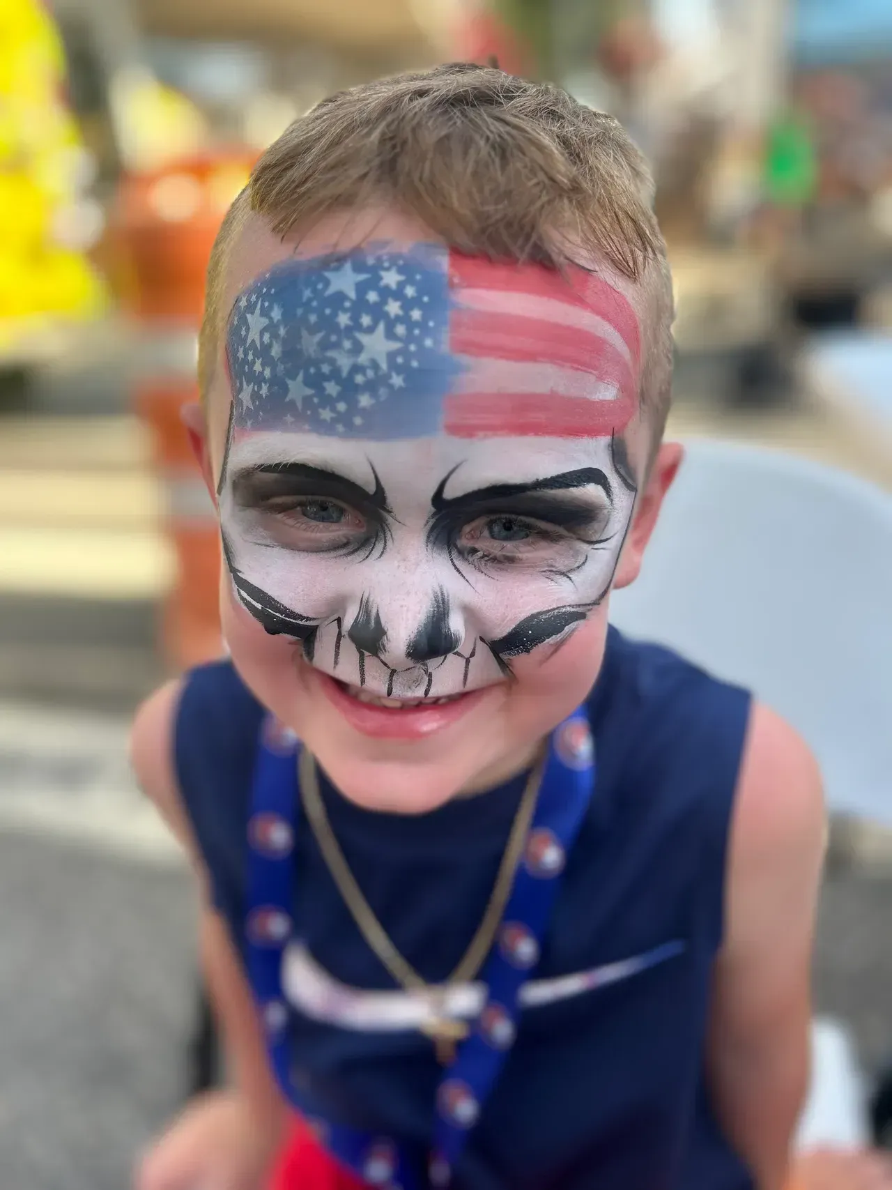 Boy with face painted as a skull and American flag, smiling outdoors.