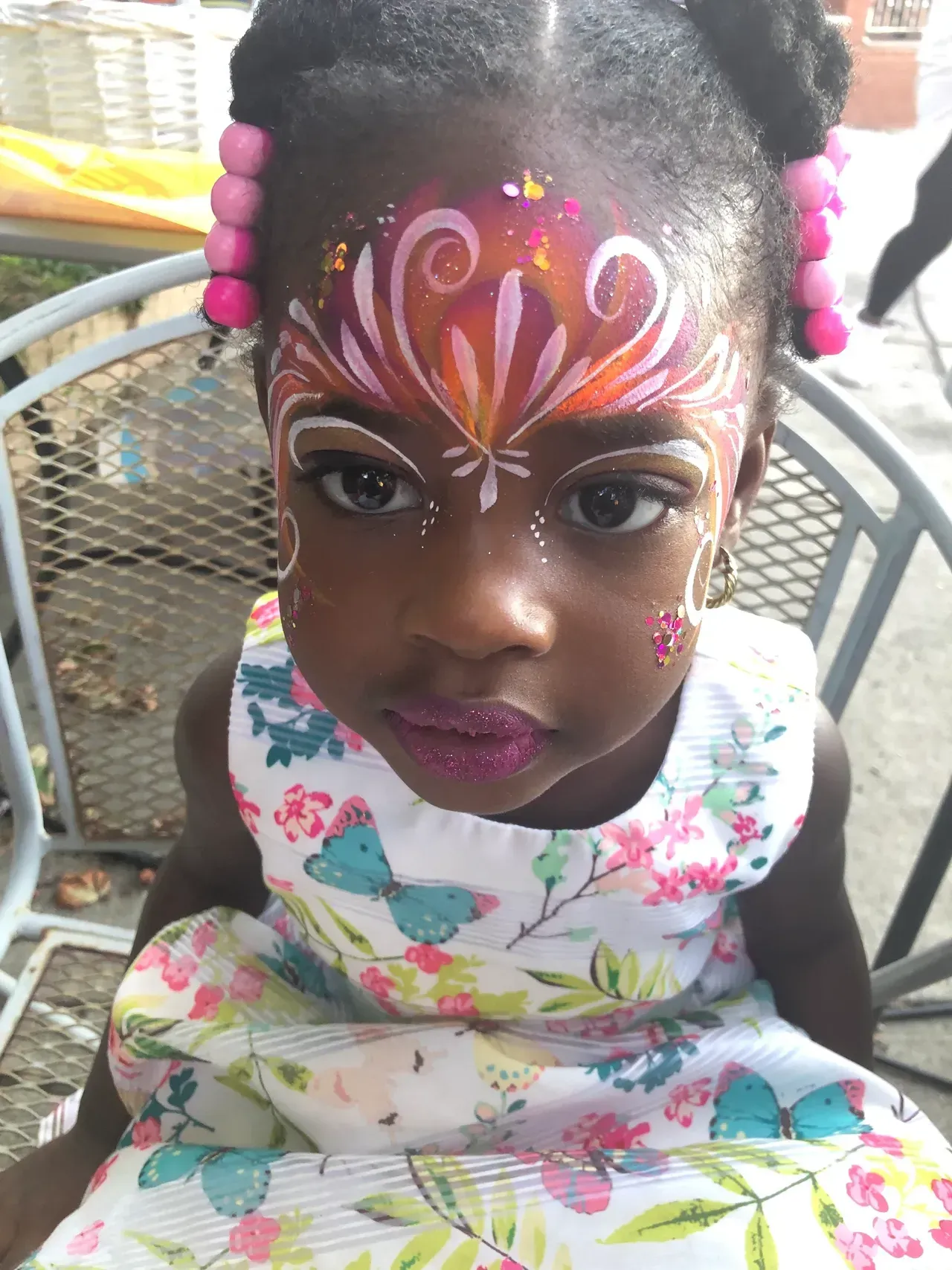 Girl with face paint and floral dress, sitting outside.