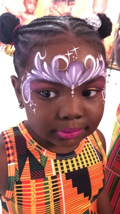 Girl with purple face paint and lipstick, wearing a patterned orange top.