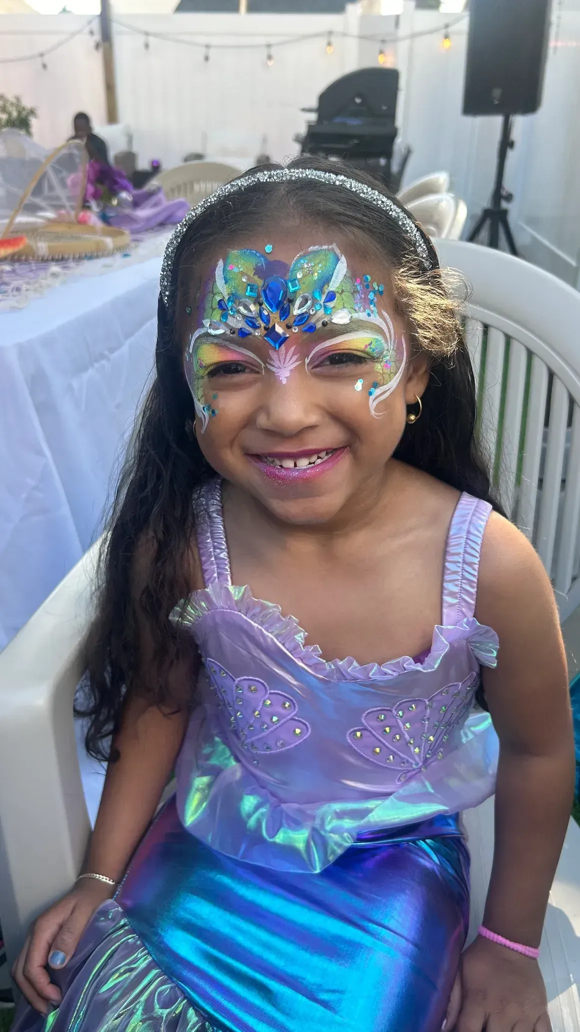 Girl in mermaid costume with face paint, smiling outdoors.