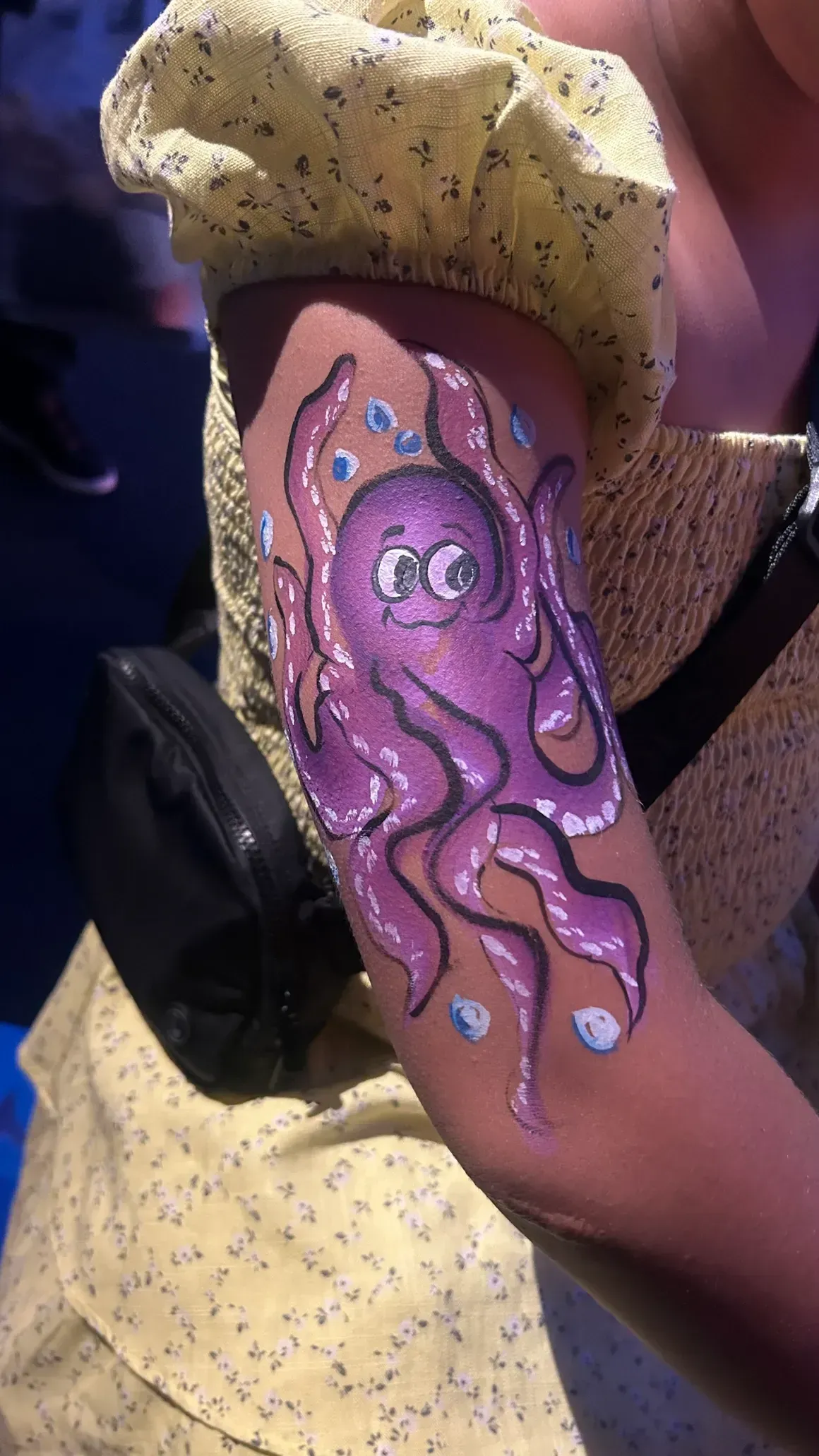 Purple octopus arm painting on a person's arm, bubbles around it, yellow floral dress.