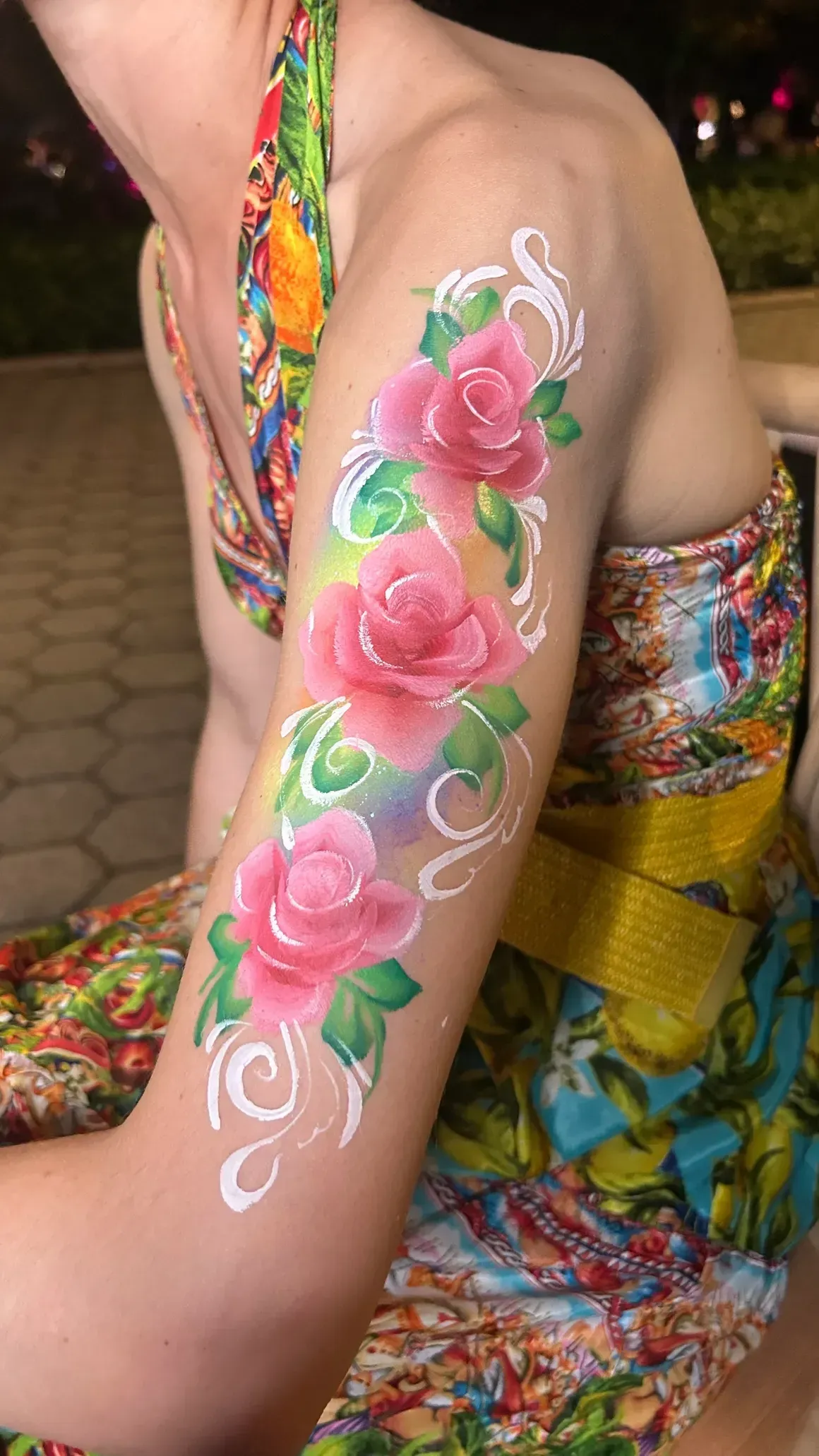 Arm with rose floral body paint. Pink roses with green leaves and white swirls on a rainbow-colored arm.