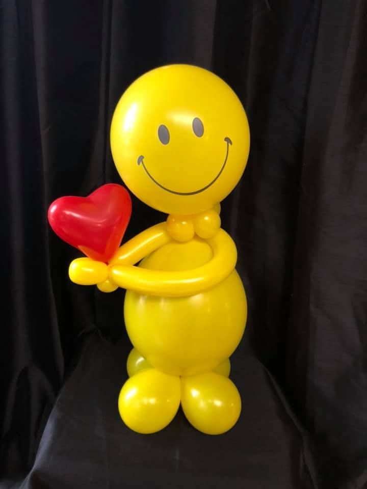 A smiley face made out of yellow balloons holding a red heart