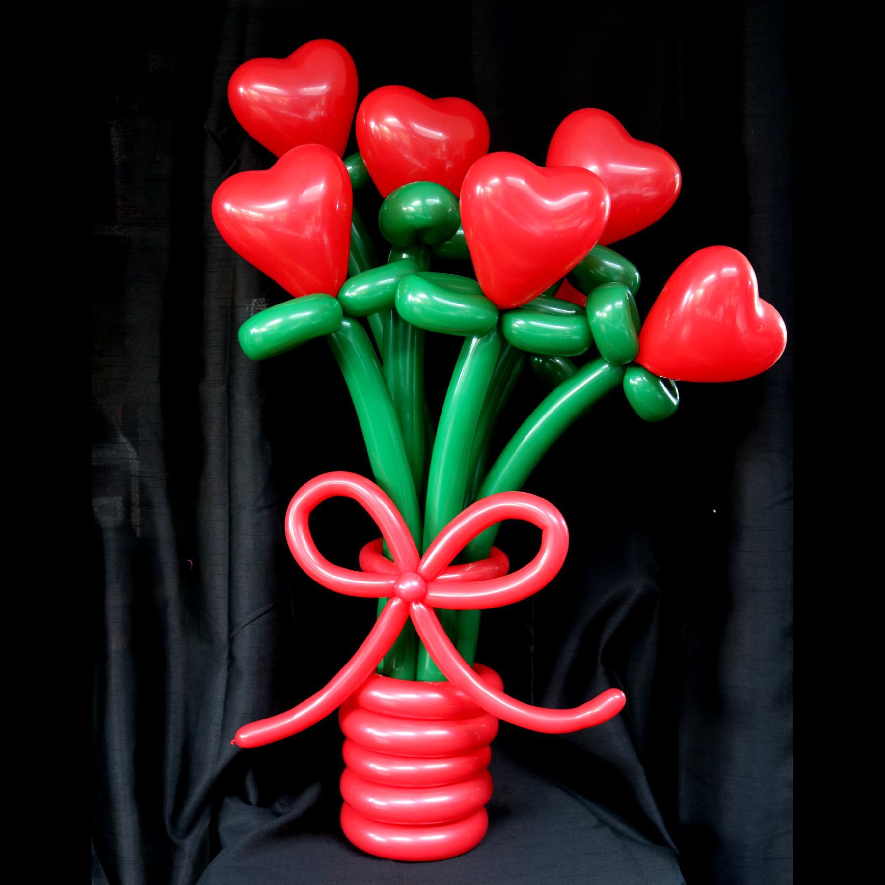 A bouquet of red and green heart shaped balloons in a red vase