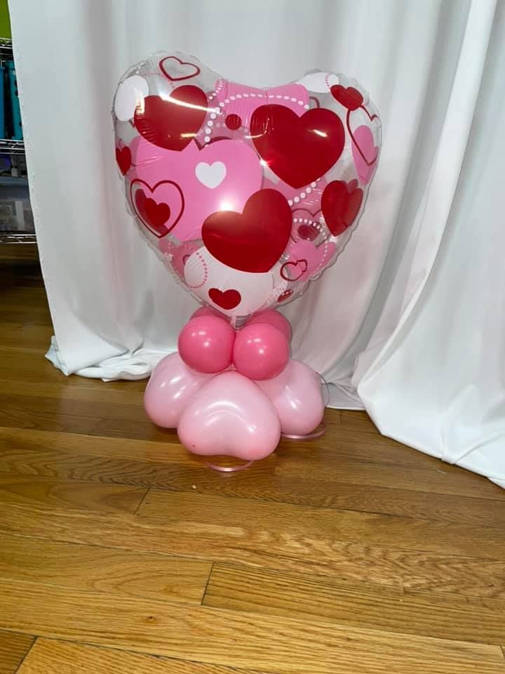 A heart shaped balloon filled with pink and red hearts is sitting on a wooden floor.