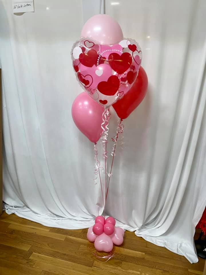 A bunch of pink and red balloons sitting on top of a wooden floor.