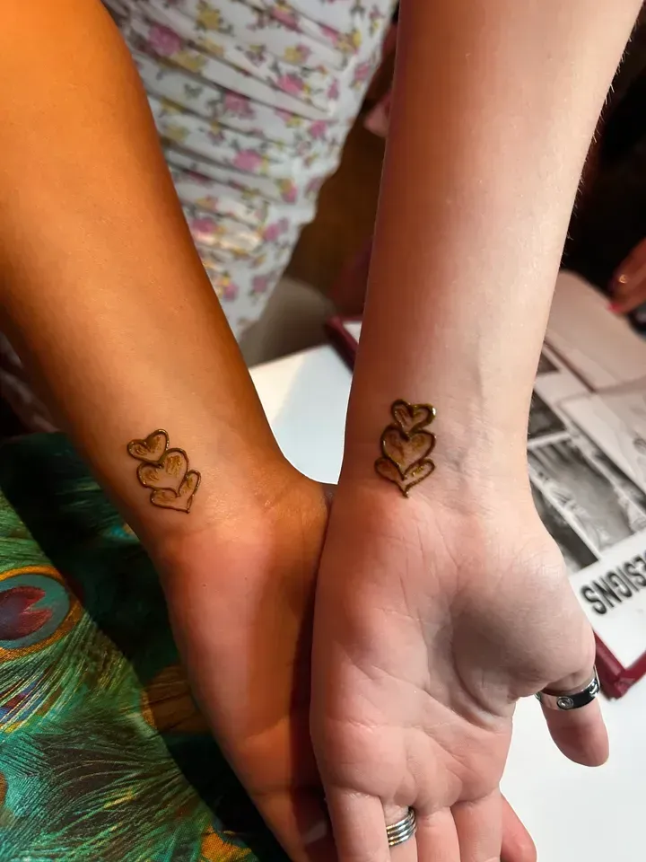 Two wrists side-by-side, each with a henna tattoo of three hearts.
