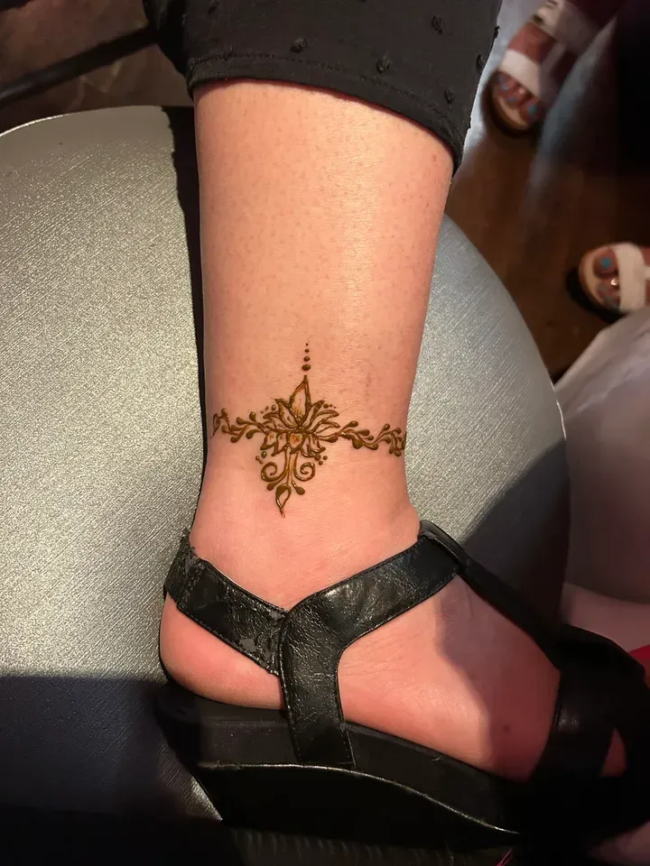 Henna ankle tattoo: brown floral design on ankle of person wearing a black sandal.