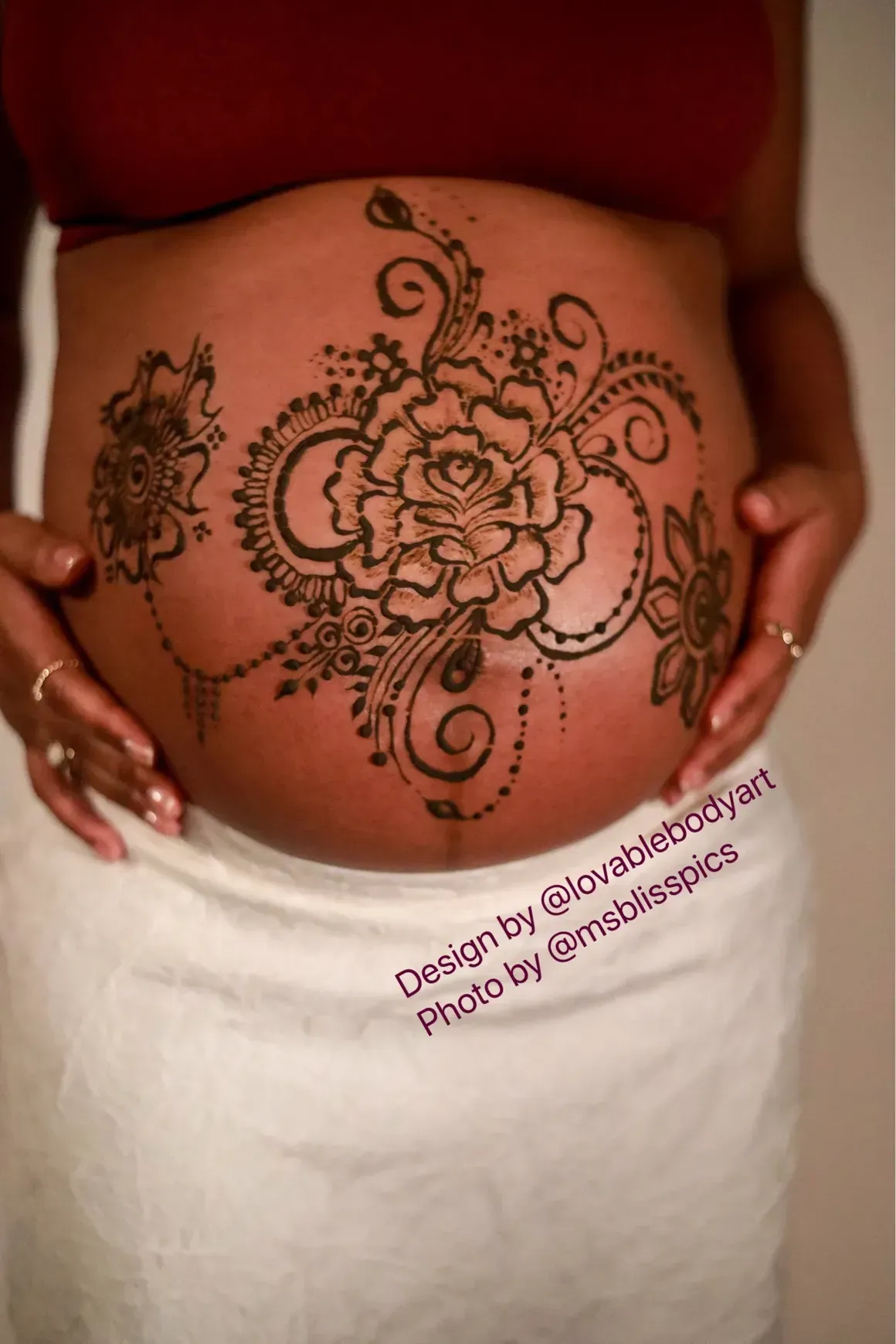 Henna design on pregnant belly featuring a large flower, swirls, and smaller floral elements.