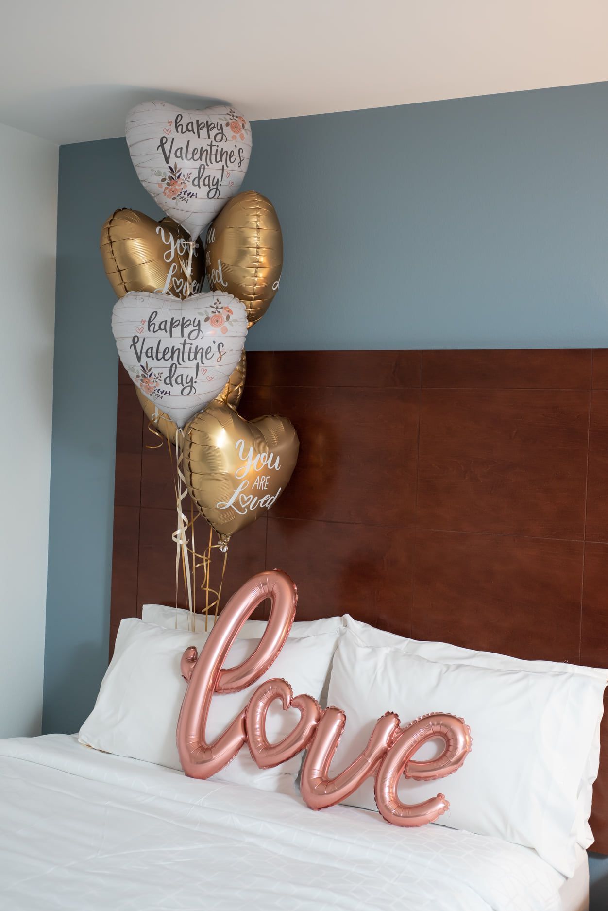 A bed with a bunch of balloons on it and a sign that says `` love ''.