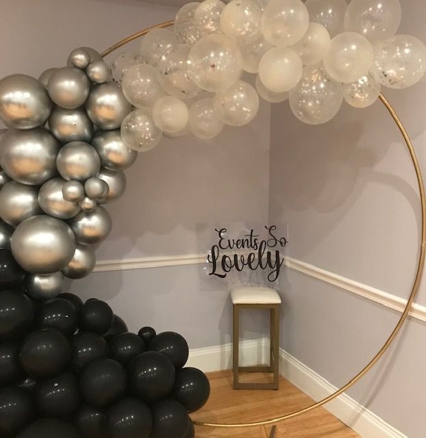 Gold hoop balloon arch with black, silver, and clear balloons. A small sign says