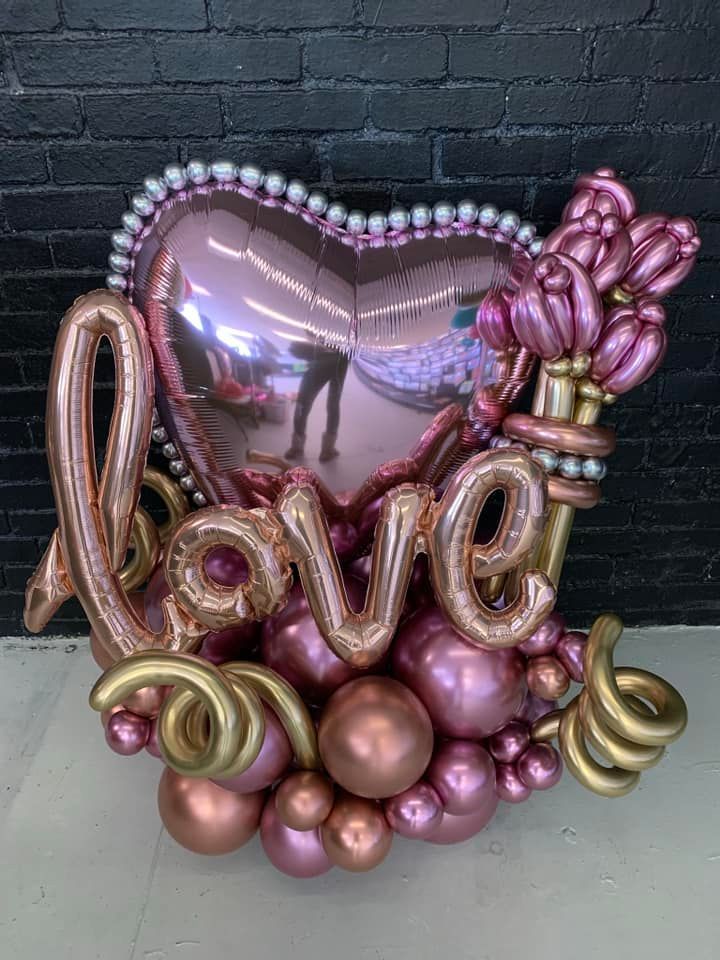 A heart shaped balloon with the word love written on it is surrounded by other balloons.