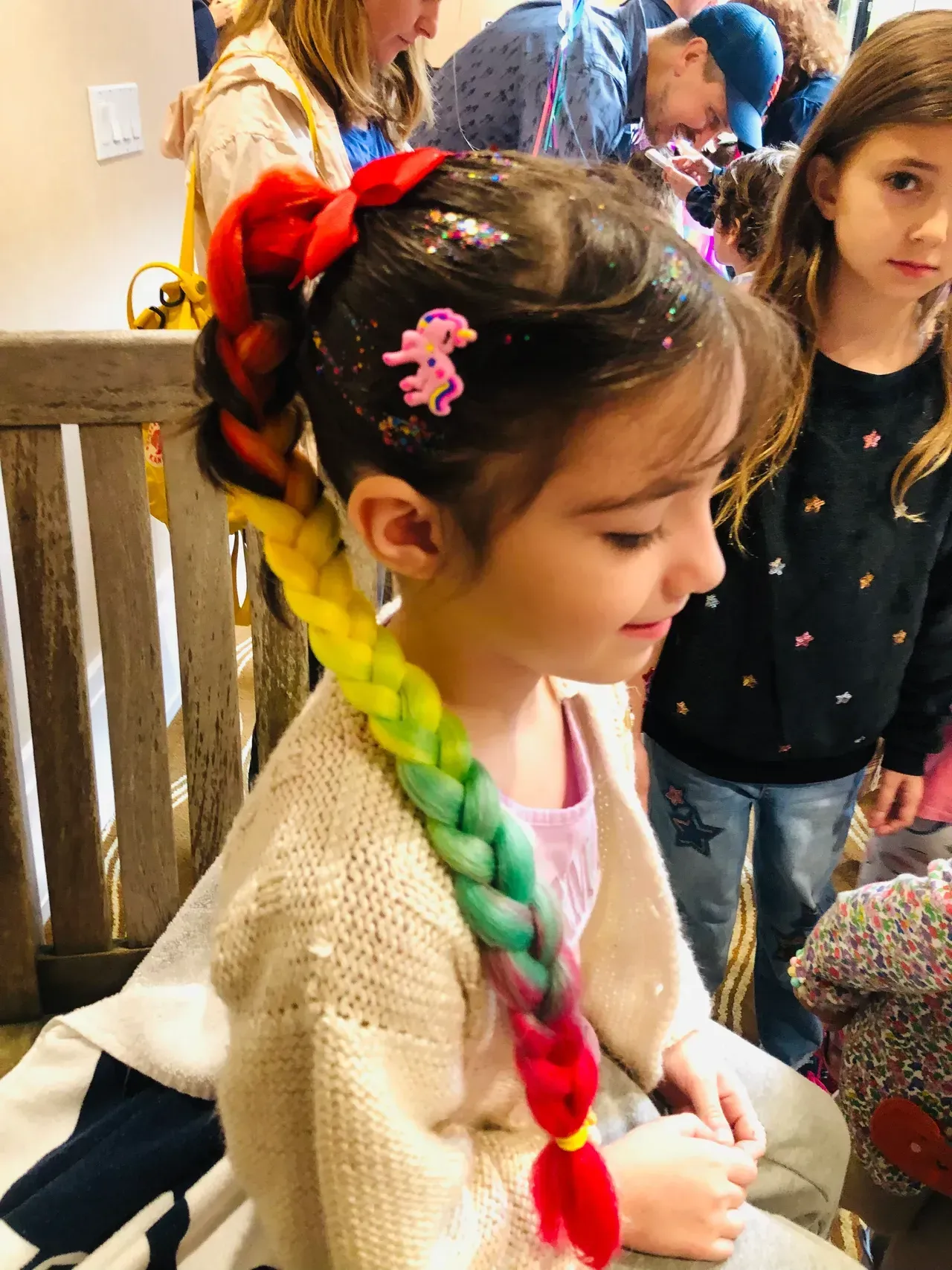 Girl with rainbow braid, glitter, and unicorn clip at event.