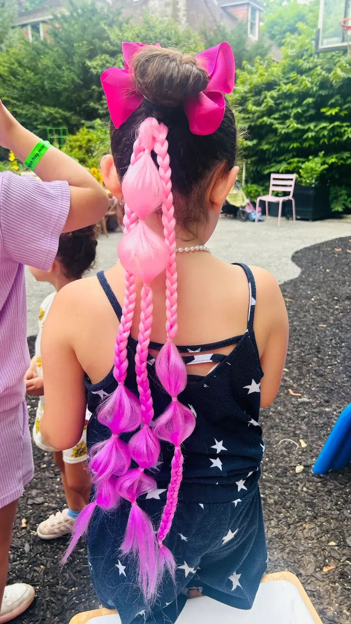 Child with pink braided hair and bows outdoors.