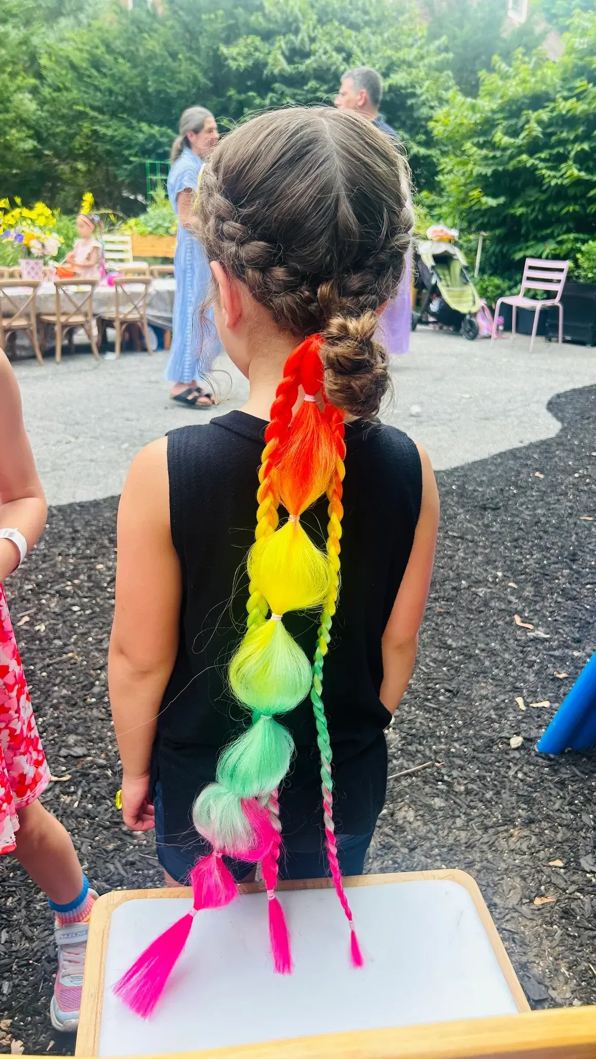 Girl with braided hair and a rainbow-colored hair accessory, standing outside.