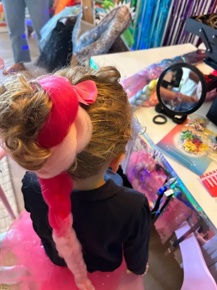 Child with pink hair accessory, facing a table with art supplies.