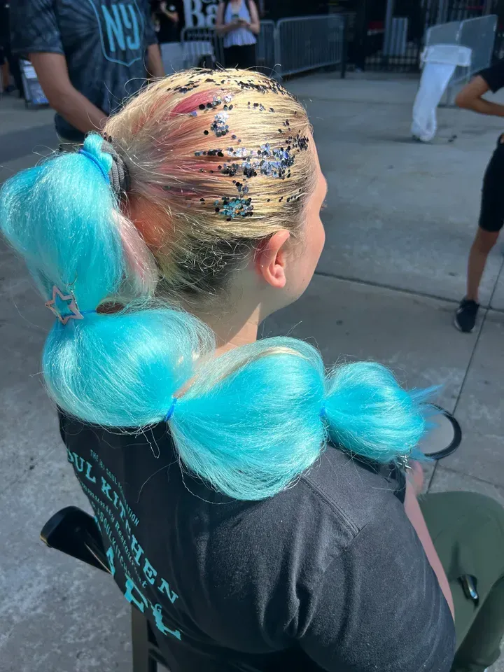 Woman with blue, bubble ponytail, blonde hair with glitter. Outdoors, sunny.