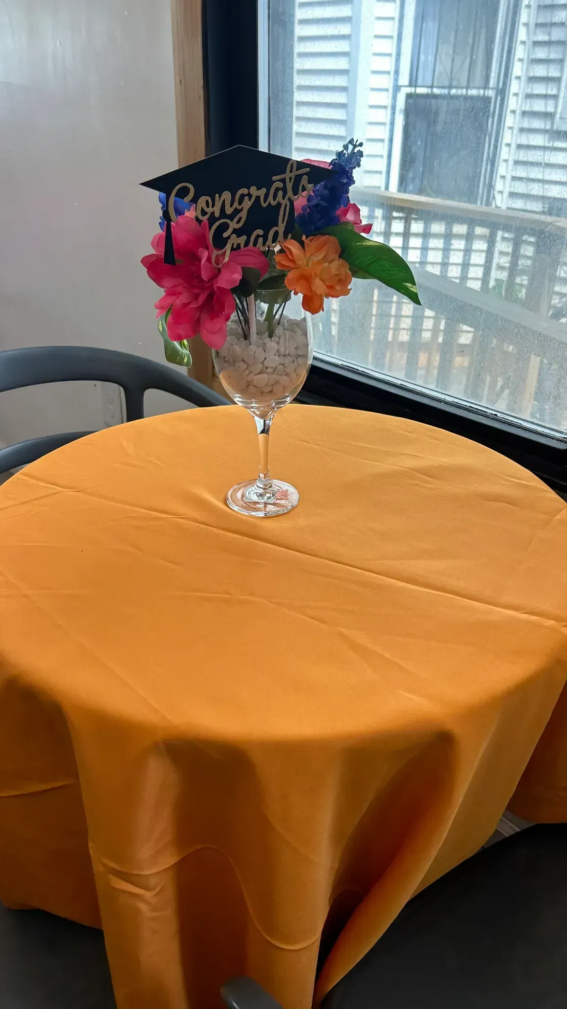 Orange tablecloth with graduation-themed flower arrangement in front of a window.