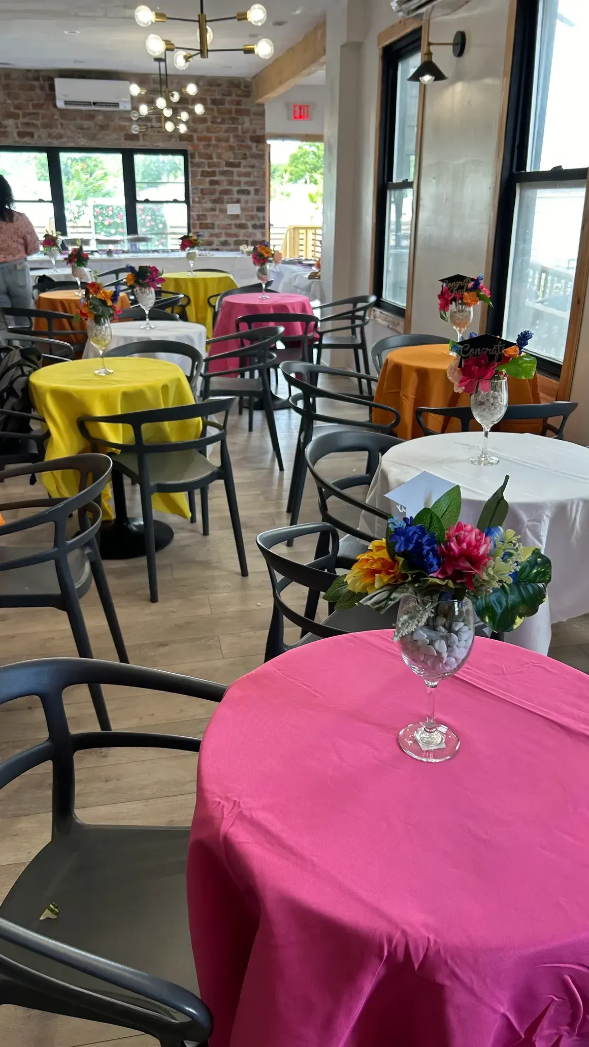 Restaurant interior with round tables draped in vibrant cloths, black chairs, and floral centerpieces.